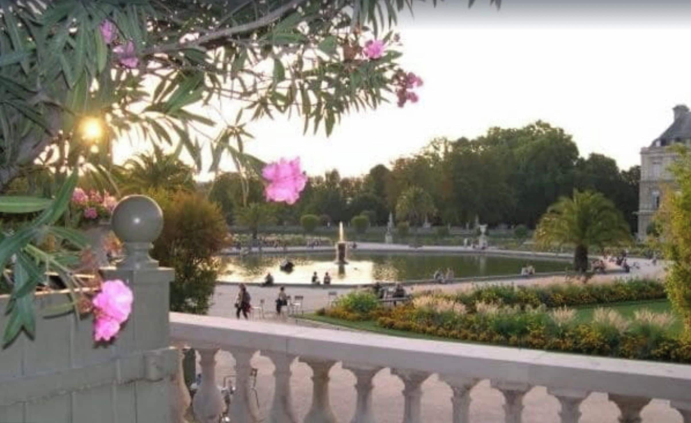 A view of a garden with a fountain, benches, and people walking.