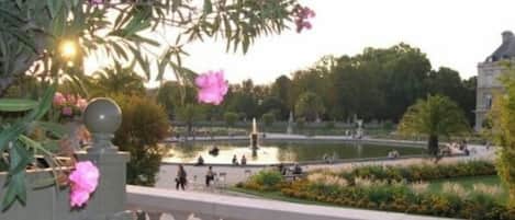A view of a garden with a fountain, benches, and people walking.