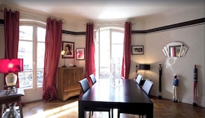 A dining room with a long table, red curtains, and a wooden cabinet. - Luxury Apartment - Jardin Du Luxembourg - Quartier Latin (Paris)