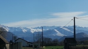 A rural road with a white building on the left, a green field, and snow-capped mountains in the background. - Mountain spirit, adventure on your doorstep (BARLEST)