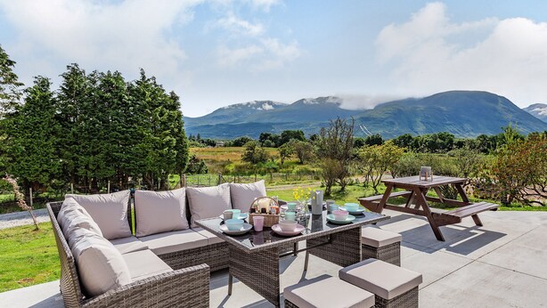 Ein Außenbereich mit Korbmöbeln und einem für das Essen gedeckten Tisch, mit Blick auf eine gebirgige Landschaft.