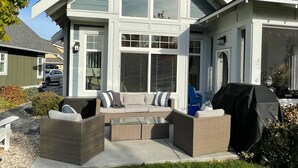 Ein modernes, zweistöckiges Haus mit überdachter Terrasse, Sitzgelegenheit im Freien und Grill.