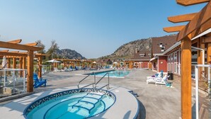 Ein Poolbereich mit mehreren Pools, Liegestühlen und Holzbauten mit Pergola.