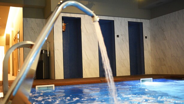Una piscina interior con una fuente de agua, paredes de azulejos y suelo de madera.