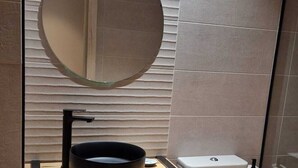 Un baño moderno con un espejo redondo, lavamanos negro y un inodoro blanco.
