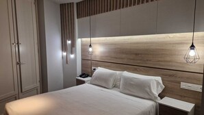 Un dormitorio moderno con cabecera de madera, una mesita de noche con lámpara y cama con ropa de cama blanca.