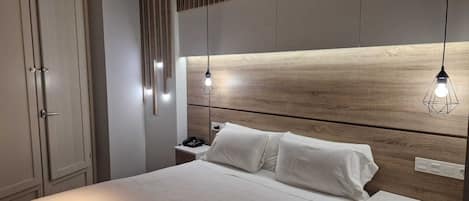 Un dormitorio moderno con cabecera de madera, una mesita de noche con lámpara y cama con ropa de cama blanca.