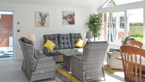 A modern living room with a grey sofa set, wicker chairs, a wooden dining table, and a chandelier.