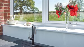 A window with a view of a tree, a brick wall, and a window sill with a pitcher, a small figurine, and a vase with flowers.