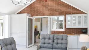 A spacious room with a sloped ceiling, a sofa, a chair, a cabinet, and a door leading to an outdoor area.