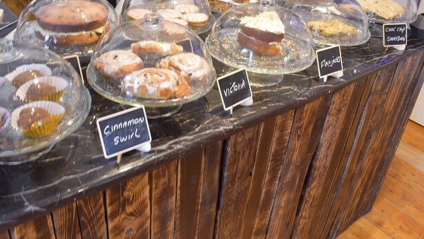 A bakery display with various pastries covered in glass domes, labeled with names like "Victoria" and "Cinnamon Swirl". - 1 bedroom accommodation in Walkerburn, near Peebles (Walkerburn, near Peebles)