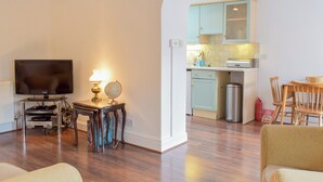 A living room with a TV, lamp, and globe on a side table, a kitchen with cabinets and a sink, and a dining area with chairs. - 1 bedroom accommodation in Walkerburn, near Peebles (Walkerburn, near Peebles)