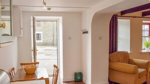 A dining area with a wooden table and chairs, a sofa, and a small green bag on the floor. - 1 bedroom accommodation in Walkerburn, near Peebles (Walkerburn, near Peebles)