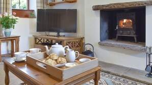 A cozy living room with a fireplace, a television, and a wooden coffee table with tea set and biscuits. - The Old Candle House (Longnor, near Buxton)