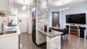 A modern kitchen with a granite countertop, stainless steel appliances, and a built-in oven. There is a dining area with a table and chairs, and a flat-screen TV mounted on the wall. - Modern apt Close to Znjan Beach, With big Terrace (Split)