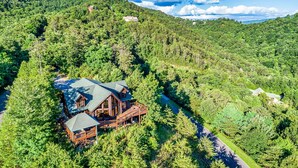 A large wooden cabin with a deck, surrounded by dense forest and hills. - 🍁SPECIAL⛄️: LUX Log Mansion w/180° VIEWS, SAUNA, & HOT TUB! 30min to Dollywood, (Sevierville)