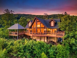 A log cabin with a large deck and a covered area, surrounded by dense forest. - 🍁SPECIAL⛄️: LUX Log Mansion w/180° VIEWS, SAUNA, & HOT TUB! 30min to Dollywood, (Sevierville)