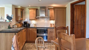A kitchen with wooden cabinets, a stove, a sink, and a dining area with a chair and table.