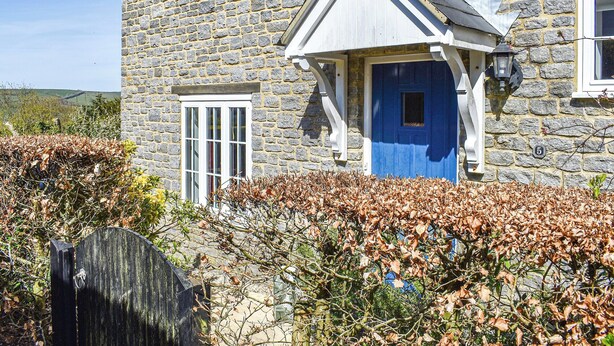 A stone house with a blue door, white window frames, and a stone wall.