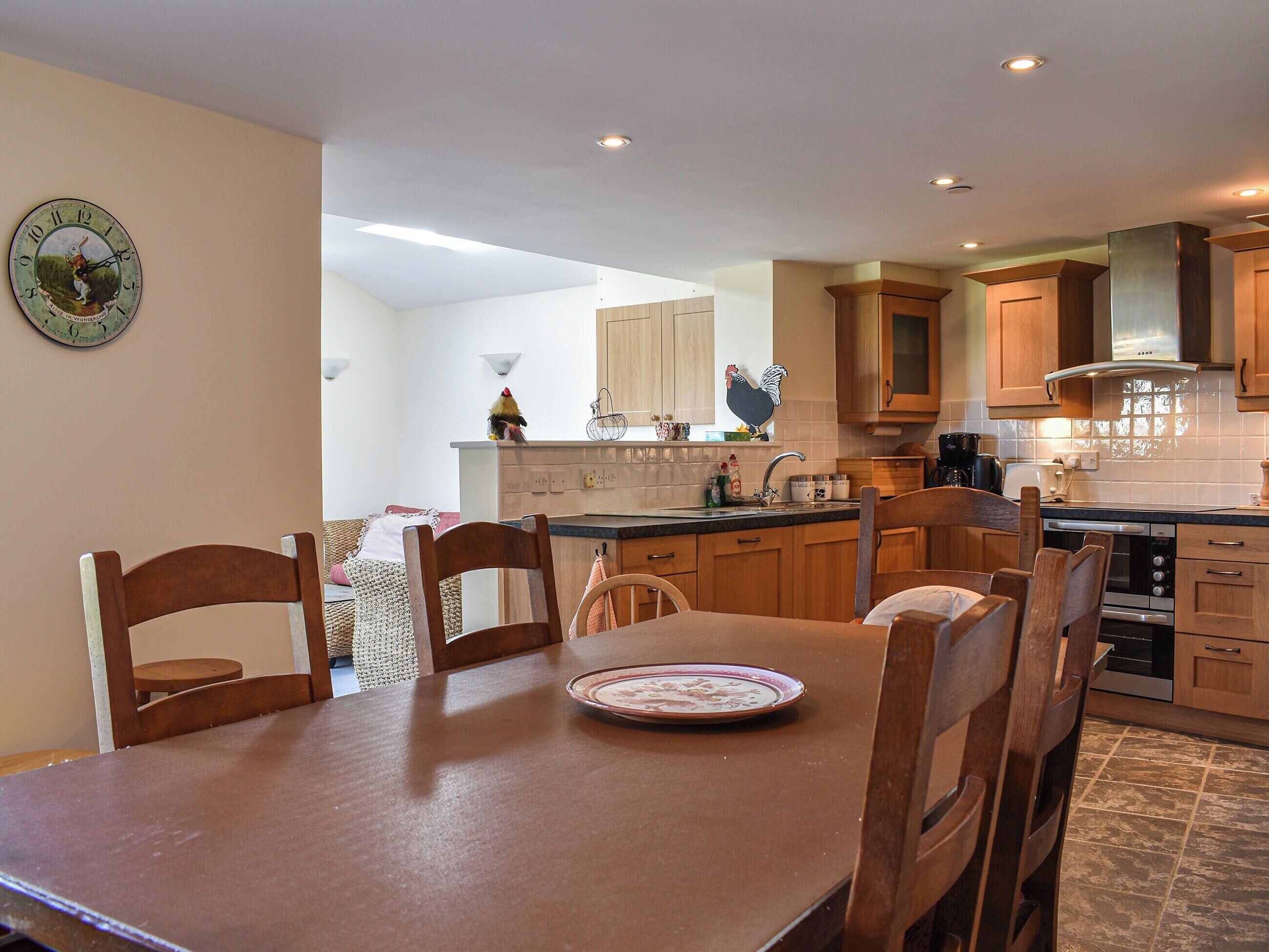 A modern kitchen with wooden cabinets, a dining table with chairs, and a wall clock.
