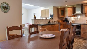 A modern kitchen with wooden cabinets, a dining table with chairs, and a wall clock.
