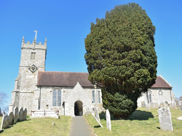 A church with a tall tower, a large tree in front, and a graveyard with headstones.