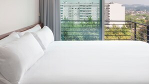 Een hotelkamer met een groot bed en uitzicht op een stadslandschap vanaf een balkon.