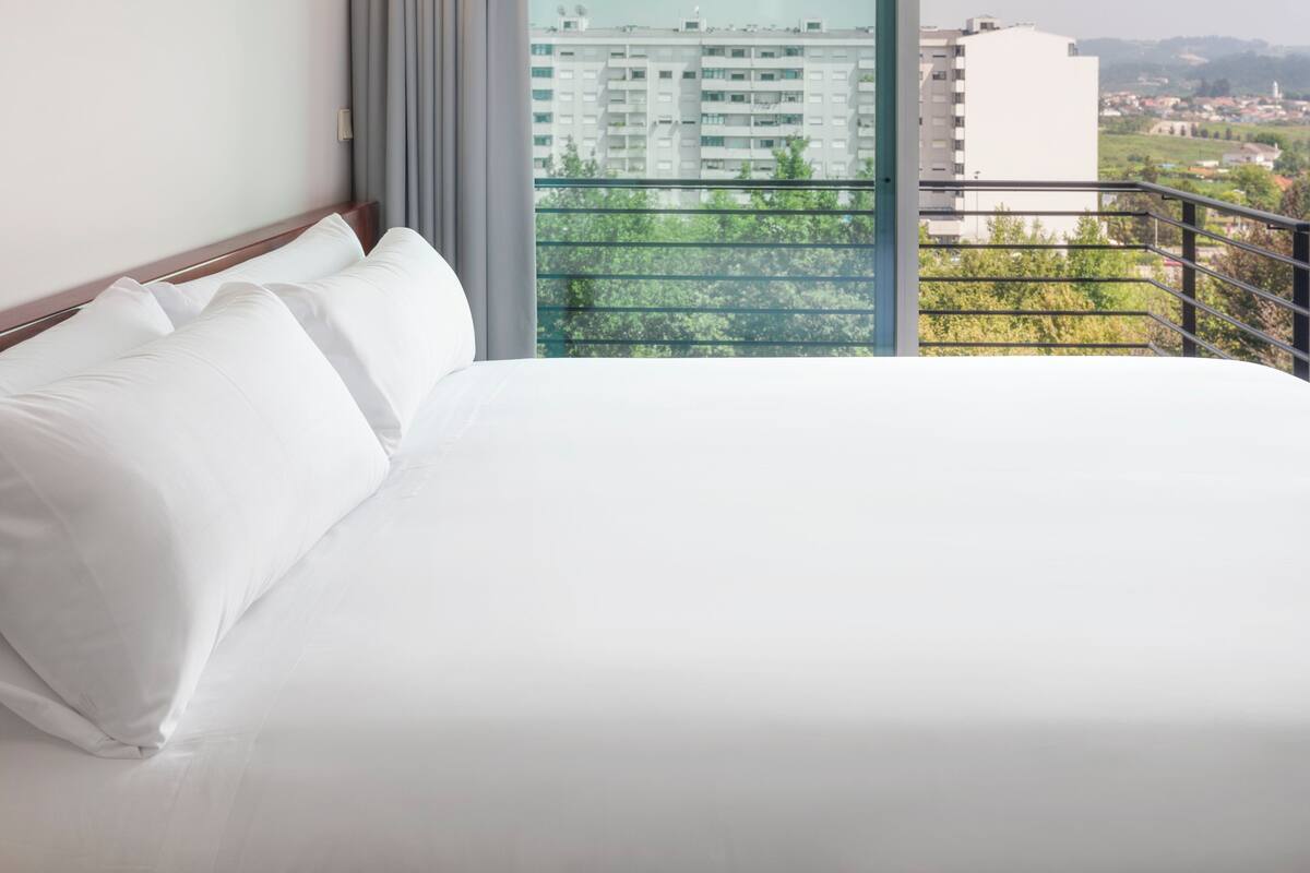 Een hotelkamer met een groot bed en uitzicht op een stadslandschap vanaf een balkon.