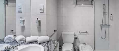 Un baño moderno con lavamanos de mármol, inodoro, bidé y ducha con mampara de vidrio.