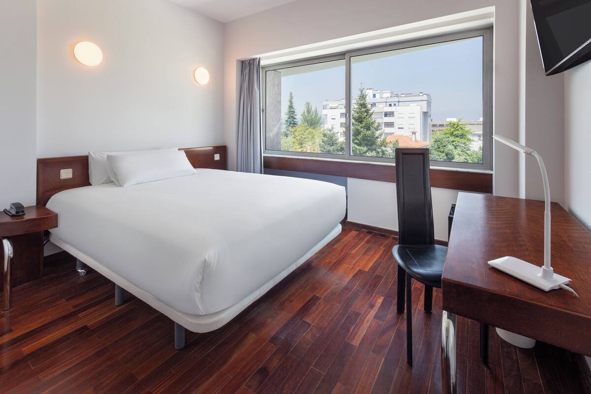 Een hotelkamer met een groot bed, een bureau, een stoel, een televisie en een raam met uitzicht over de stad.