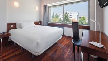 Una habitación de hotel con una cama grande, un escritorio, una silla, un televisor y una ventana con vista a la ciudad.