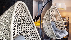 Twee hangstoelen met grijze kussens in een modern interieur met een gepolijste vloer en een trap op de achtergrond.