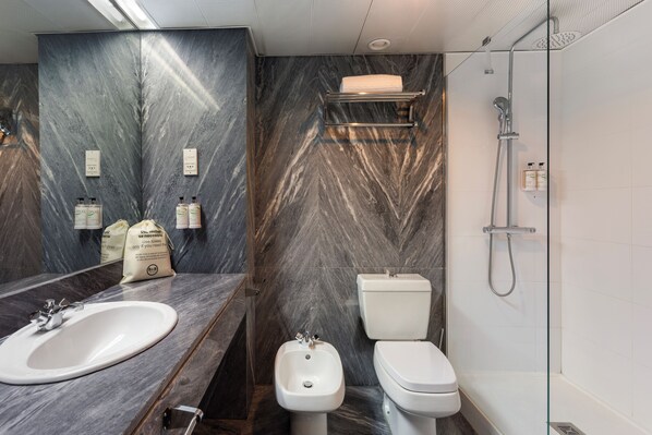 A modern bathroom with a marble vanity, a bidet, a toilet, and a glass-enclosed shower.