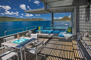 Une terrasse avec des sièges extérieurs, une table avec un jeu de société et une vue sur la mer et les collines.