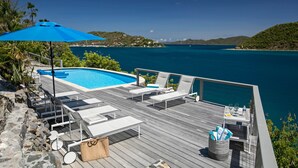 Una terraza de madera con sillones de descanso, una piscina y vista al mar.