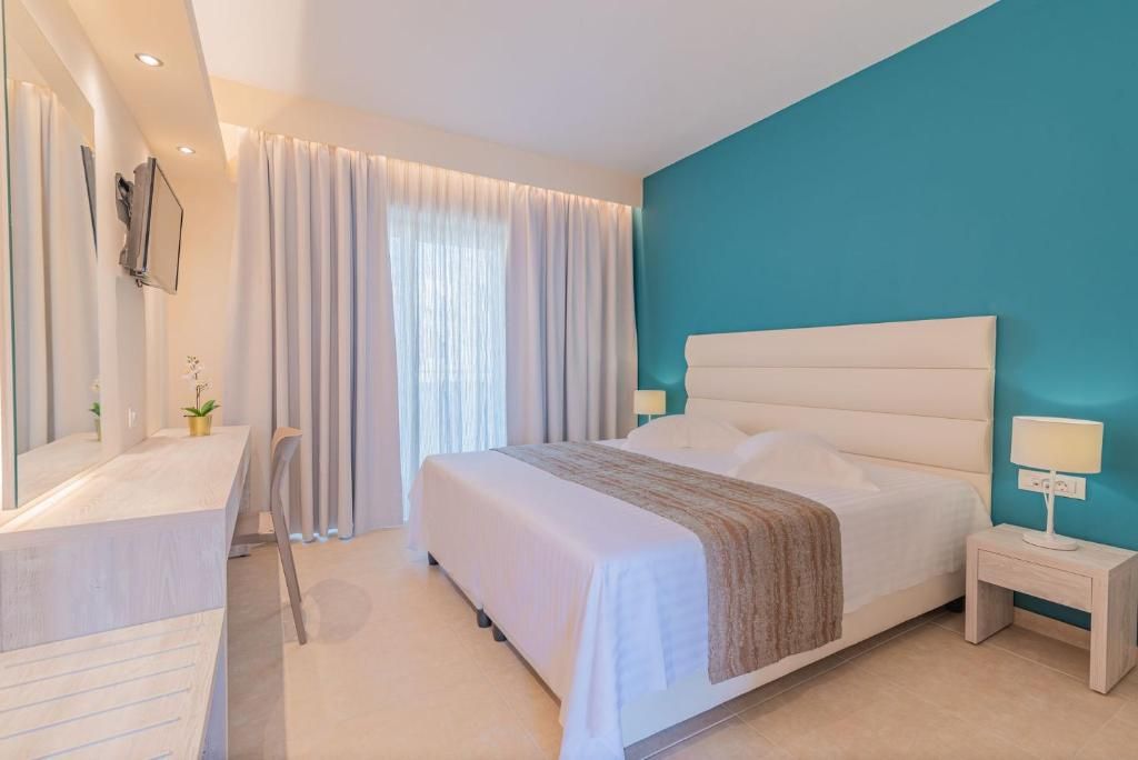 Un dormitorio moderno con una cama grande, una mesita de noche con lámpara, un escritorio con silla y un amplio ventanal con cortinas.