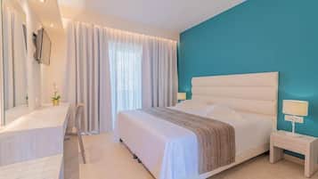 Un dormitorio moderno con una cama grande, una mesita de noche con lámpara, un escritorio con silla y un amplio ventanal con cortinas.
