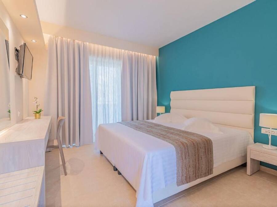 Un dormitorio moderno con una cama grande, una mesita de noche con lámpara, un escritorio con silla y un amplio ventanal con cortinas.
