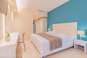 Una habitación de hotel moderna con una cama grande, un escritorio con una silla, una mesita de noche pequeña y un televisor.