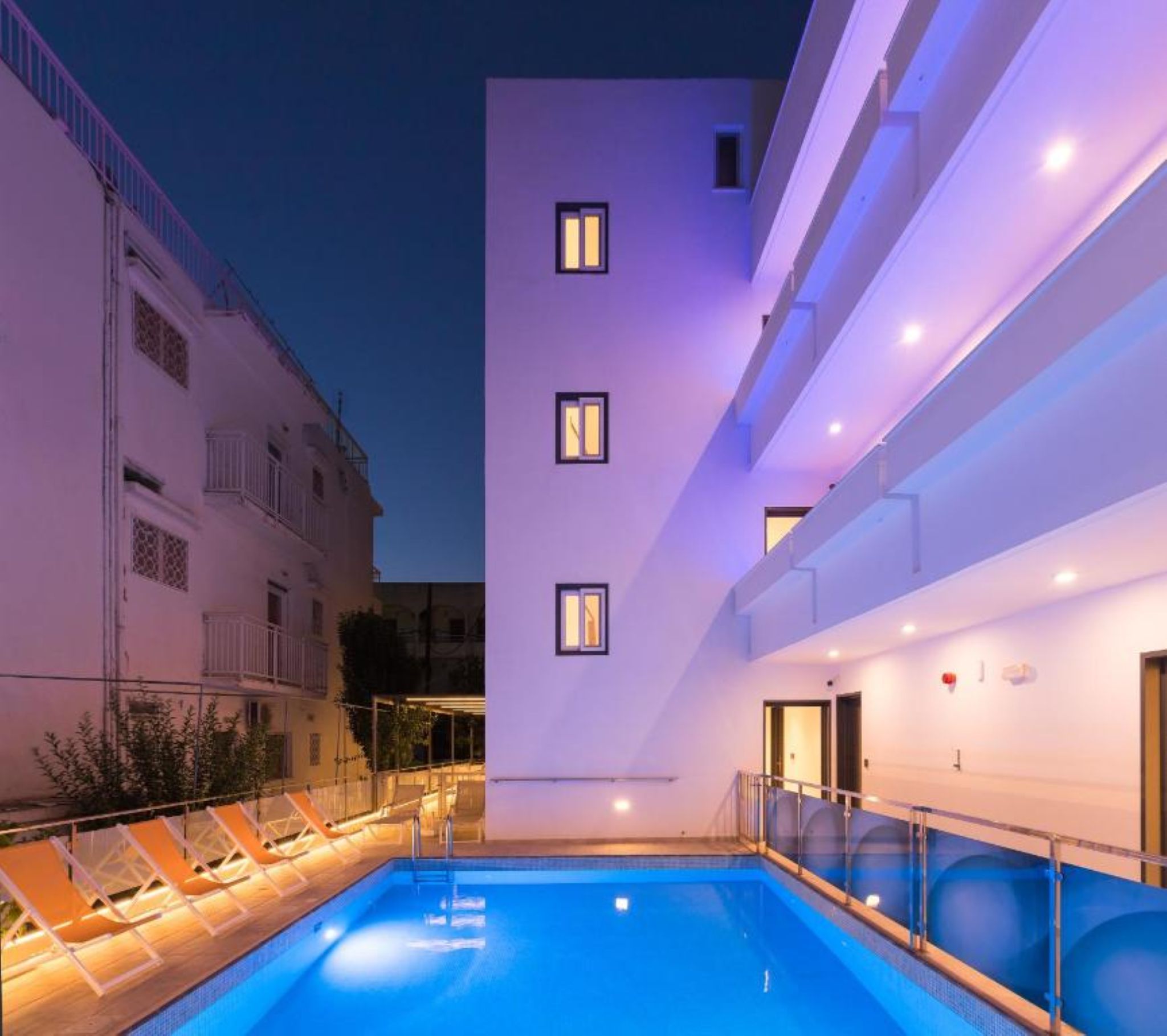 A modern building with a pool area, including lounge chairs and a clear blue pool.