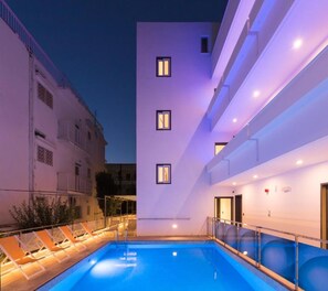 A modern building with a pool area, including lounge chairs and a clear blue pool.