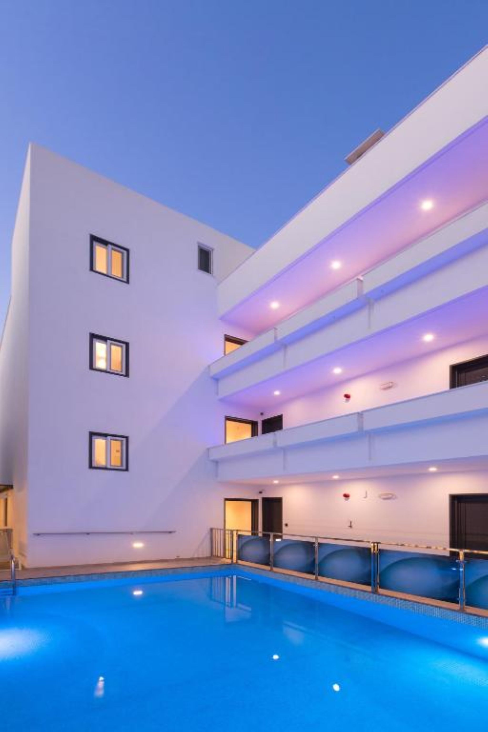 A modern hotel with a swimming pool, multiple balconies, and a clean, white facade.
