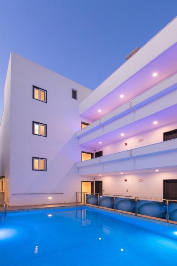A modern hotel with a swimming pool, multiple balconies, and a clean, white facade.