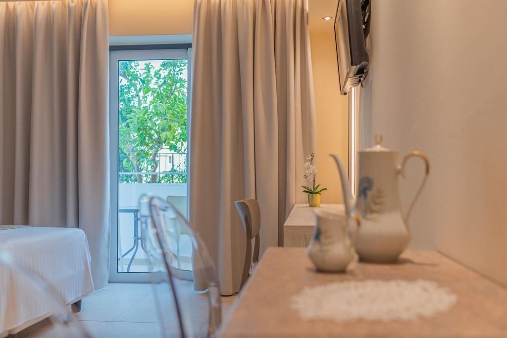 A hotel room with a bed, a table with a vase, a chair, and a view of greenery outside.