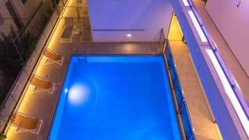 Una piscina en la azotea con superficie de agua azul cristalina, rodeada por un edificio moderno con balcones y fachada bien iluminada.