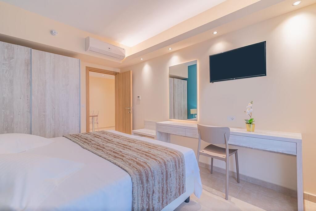 A modern bedroom with a large bed, a desk, and a TV mounted on the wall.