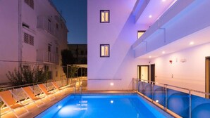 A modern building with a pool area, including lounge chairs and a clear blue pool. - Christa (Kos)