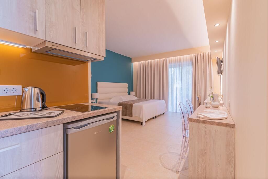 Habitación de hotel moderna con kitchenette, cama con ropa blanca, baño con ducha y vistas al exterior.