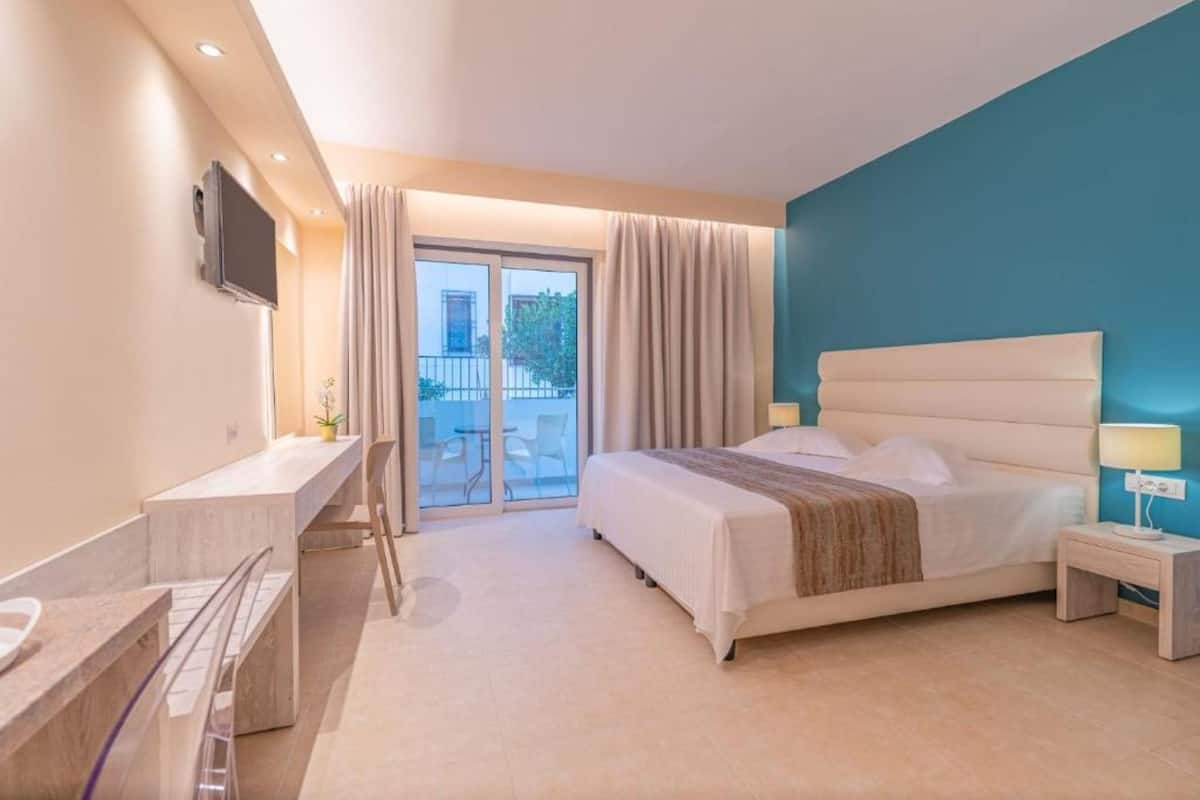 A hotel room with a bed, a desk, a TV, and a balcony with curtains.