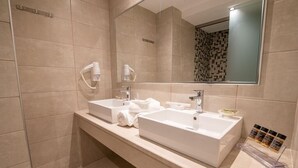 A modern bathroom with two sinks, a large mirror, and a shower area. - Christa (Kos)